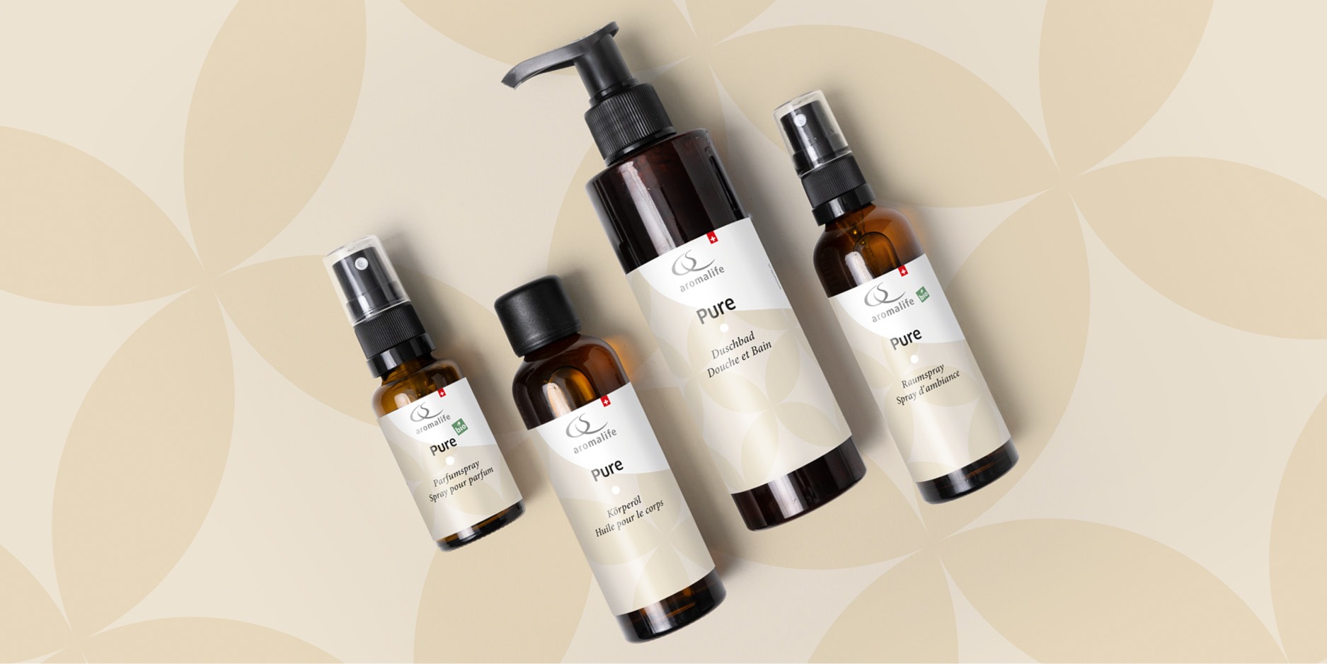 Aromalife PURE-Produkte Parfumspray, Körperöl und Duschbad liegen auf einem hellen Boden mit Kreismuster.
