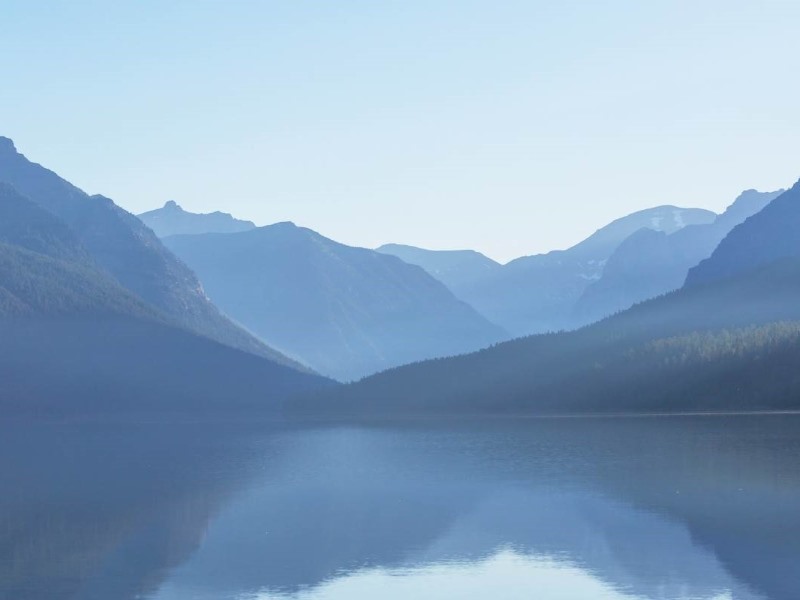 Blick auf einen Bergsee umgeben von Bergen mit einem Violett-Stich