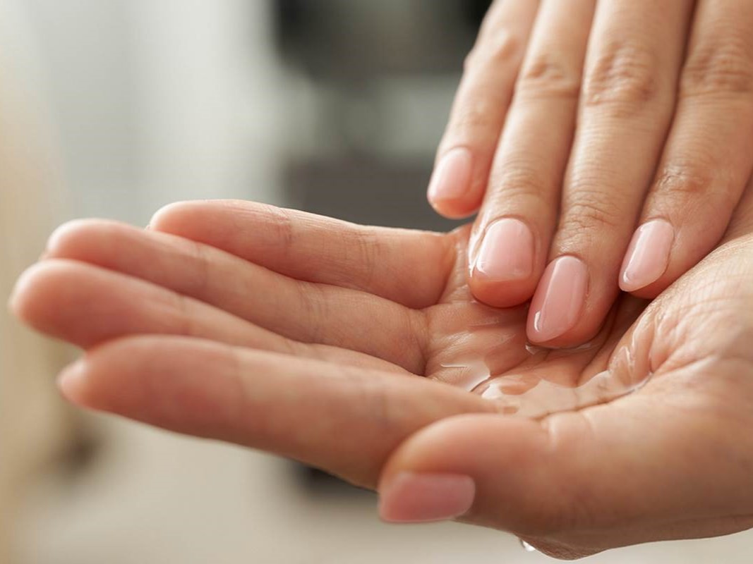 Hand massiert Körperöl auf eine andere Hand ein.