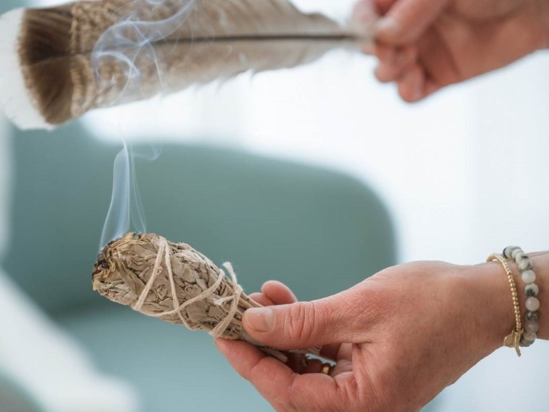 Hand hält Räucherbündel in der einen Hand und in der anderen Hand eine Truthahnfeder