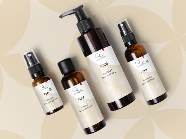 Aromalife PURE-Bodylotion, -Raumspray, -Parfumspray und -Massageöl liegen auf einem hellen Boden mit Kreismuster
